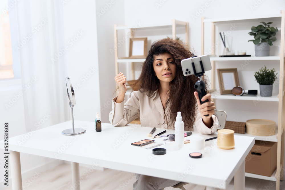 MODERN WORK. Enjoyed tanned handsome curly Latin beauty blogger in linen shirt sit on chair in home white interior. Copy space Mockup Banner. Influencer record video review blog using smartphone MODERN WORK. Enjoyed tanned handsome curly Latin beauty blogger in linen shirt sit on chair in home white interior. Copy space Mockup Banner. Influencer record video review blog using smartphone