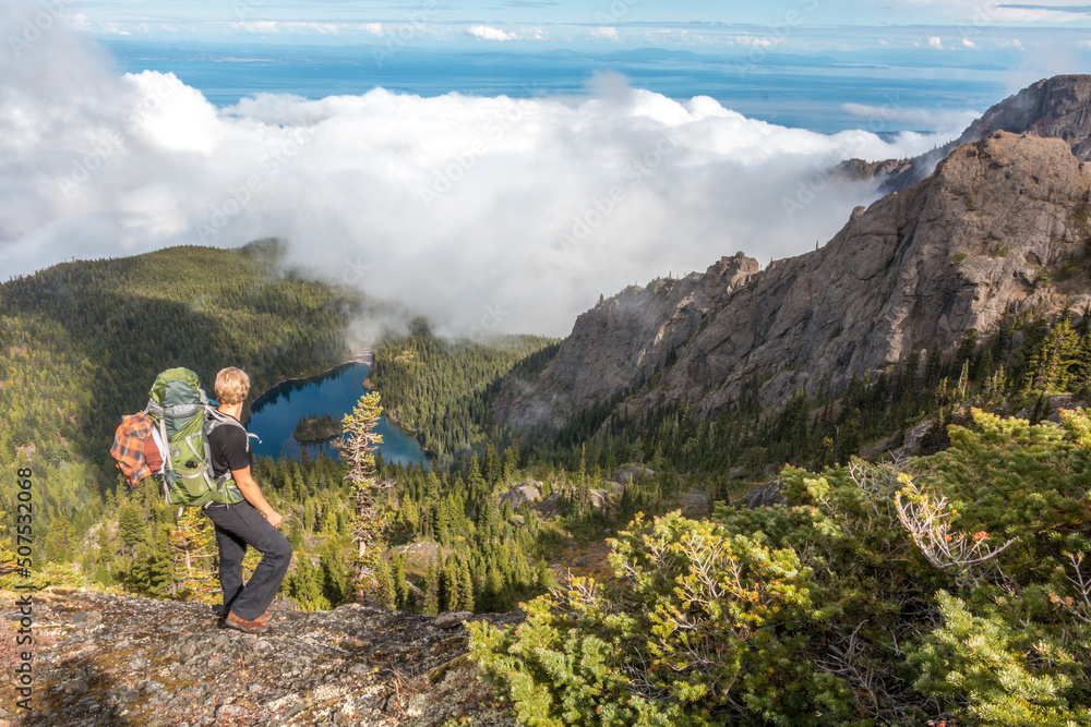 Hiker overlooking mountain lake and forest in summer with sea fog encroaching