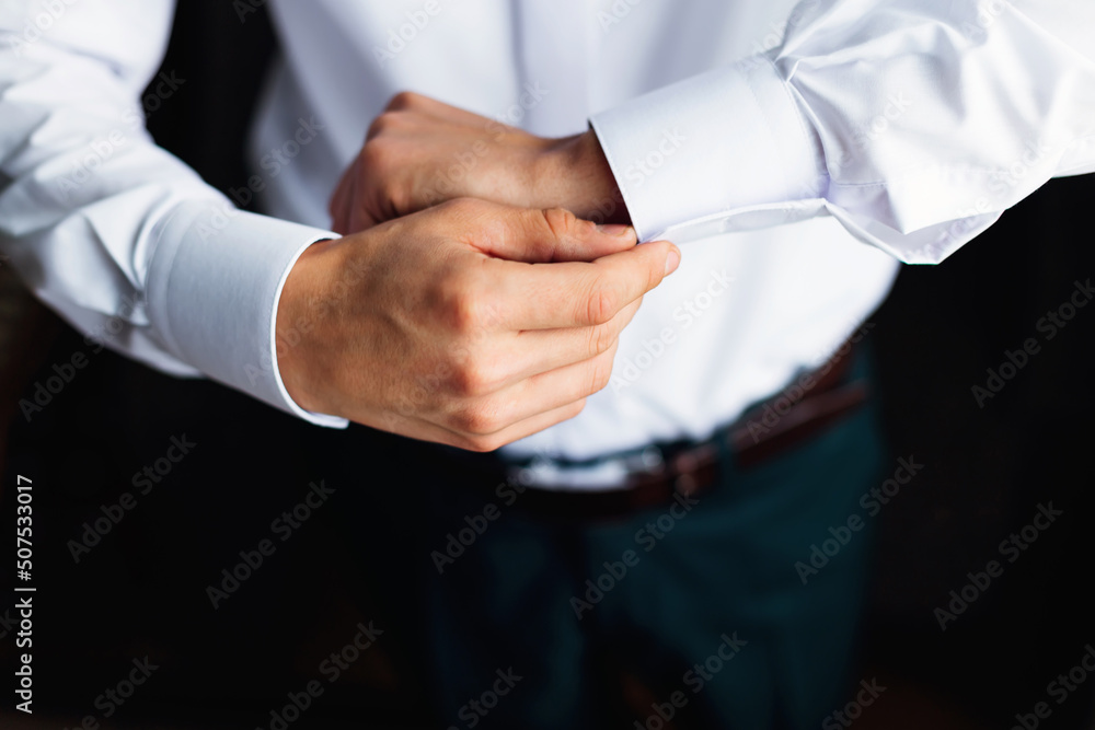 A man fastens a button (cufflinks) on a white shirt. Close-up of button fastening on the cuff of a man's shirt