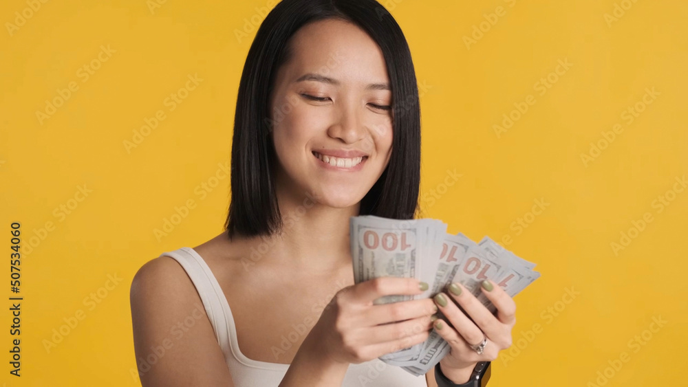 Young Asian businesswoman counting money and smiling at camera over yellow background Young Asian businesswoman counting money and smiling at camera over yellow background