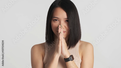 Young Asian woman making a wish holding hands together over gray background. May dreams come true