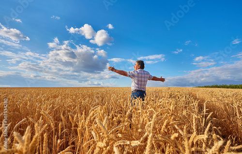 Happy farmer proudly standing in wheat field. Agronomist wearing corporate uniform, looking at camera on farmland.