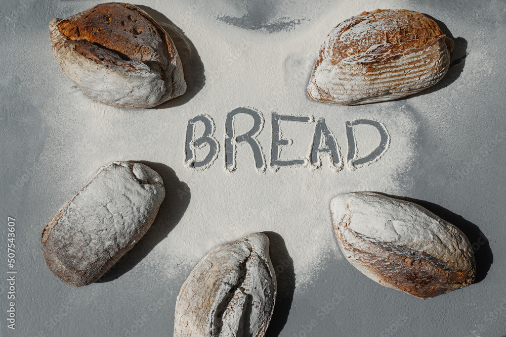 Naklejka premium The word Bread in flour between several loaves of bread on a gray background.