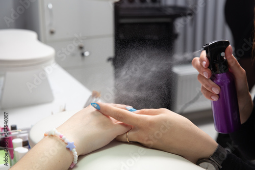 Manicurist sprays antiseptic on the nails before treating old acrylic nails.