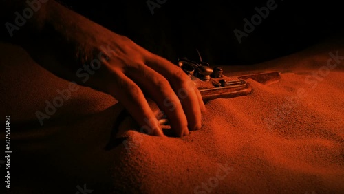 Pirate Picks Up Pistol From The Sand In Firelight photo