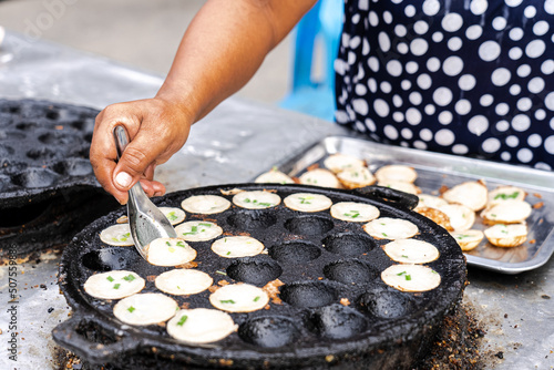 Thai Woman Making Thai Coconut Puddings or Kanom Krok With Topping in Morning