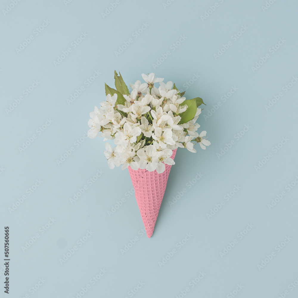 White flower in ice cream cone on pastel blue background. Flat lay. Summer tropical concept.