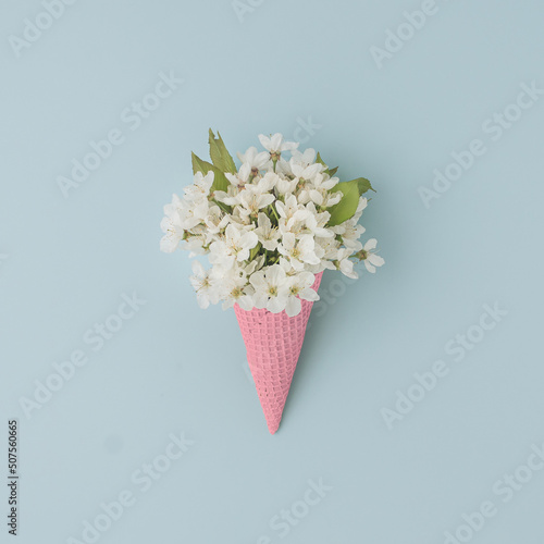 Fototapeta Naklejka Na Ścianę i Meble -  White flower in ice cream cone on pastel blue background. Flat lay. Summer tropical concept.