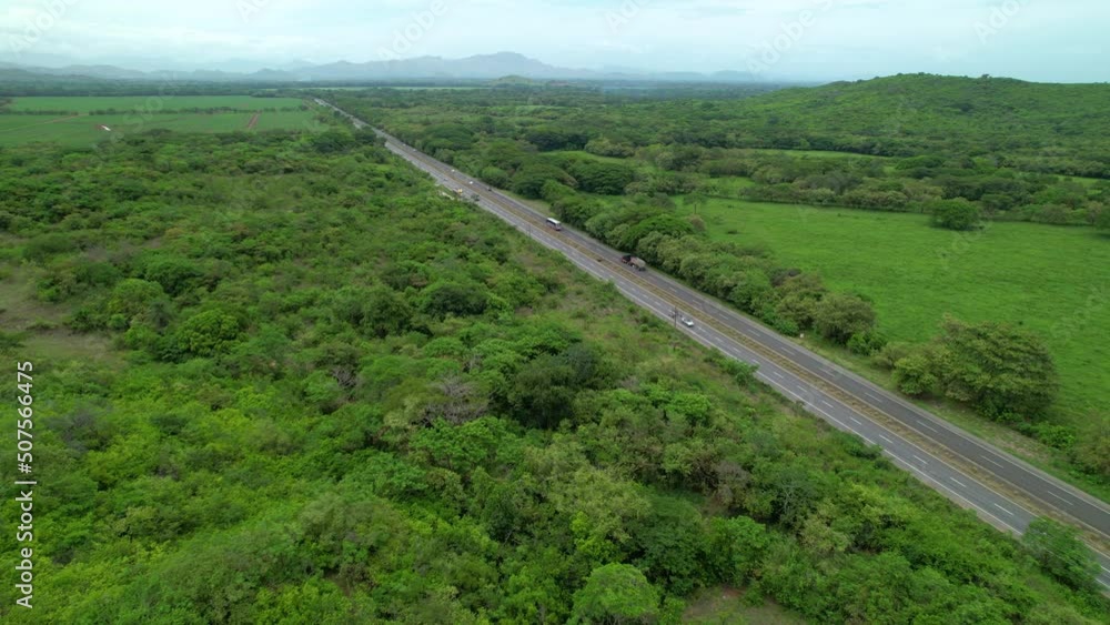 AERIAL: Big 18-wheelers and cars drive along the scenic Panamerican highway. Lush jungle foliage surrounds a busy freeway in a rural part of Panama. Drone shot of the world famous Panamericana. AERIAL: Big 18-wheelers and cars drive along the scenic Panamerican highway. Lush jungle foliage surrounds a busy freeway in a rural part of Panama. Drone shot of the world famous Panamericana.