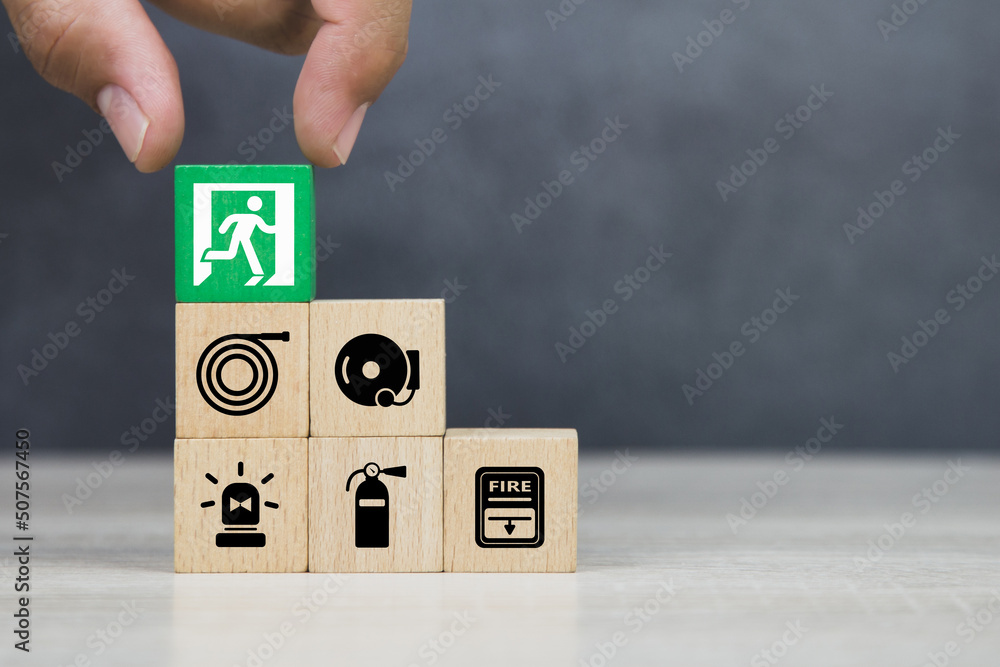 Hand choose wooden block stack with door exit sing or fire escape and fire prevent icon with fire extinguisher and emergency protection symbol for safety and rescue in the building. Hand choose wooden block stack with door exit sing or fire escape and fire prevent icon with fire extinguisher and emergency protection symbol for safety and rescue in the building.