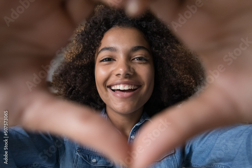 Slika na platnu Closeup portrait excited smiling Black female vlogger influencer look at web cam in heart shape of fingers say I love you to audience