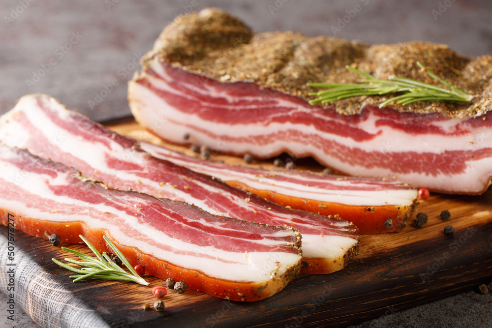 Dry-cured pork belly bacon with spices and rosemary close-up on a wooden board on the table. horizontal