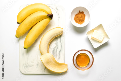 Ingredient for fried bananas with honey cinnamon butter sauce; Cavendish bananas, cinnamon, butter and honey. Top view on white table background. Make this easy banana dessert recipe.