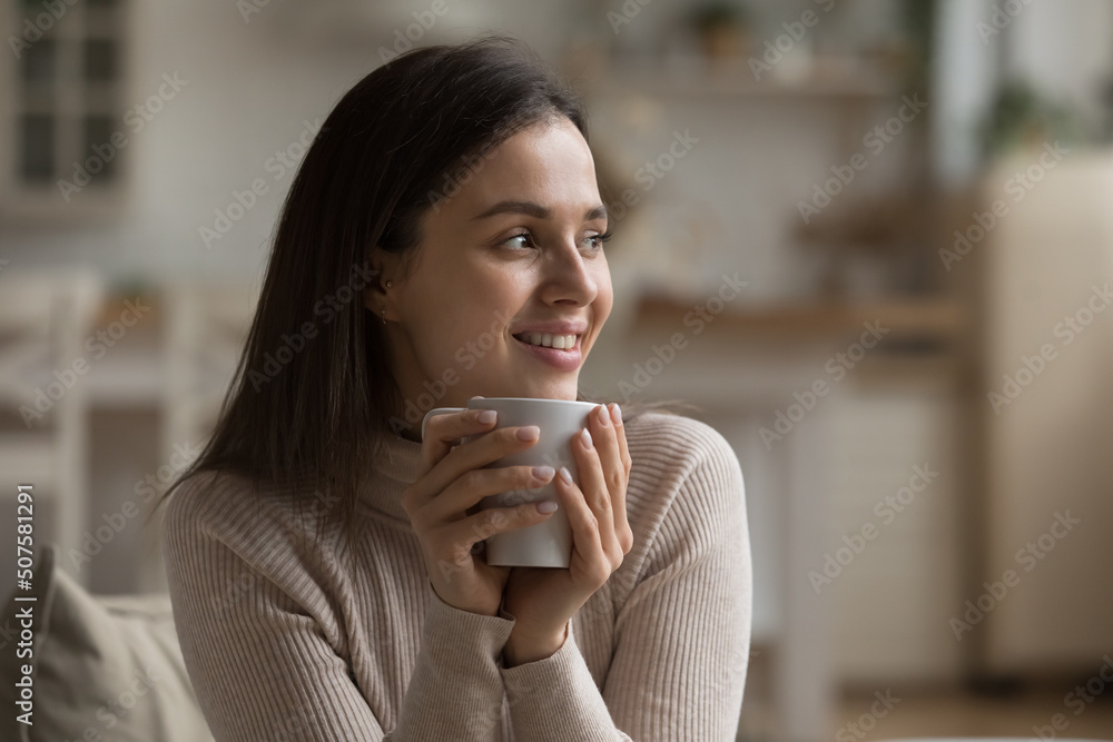 Cheerful dreamy girl holding mug of hot beverage, looking away in deep good thoughts, smiling, dreaming, enjoying aromatic herbal tea, smelling morning coffee, warming hands Cheerful dreamy girl holding mug of hot beverage, looking away in deep good thoughts, smiling, dreaming, enjoying aromatic herbal tea, smelling morning coffee, warming hands