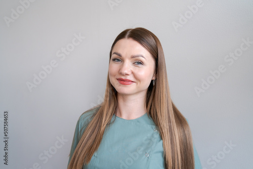 Portrait professional beautician smiling young woman in green uniform confident in medical aesthetic office looking at camera closeup