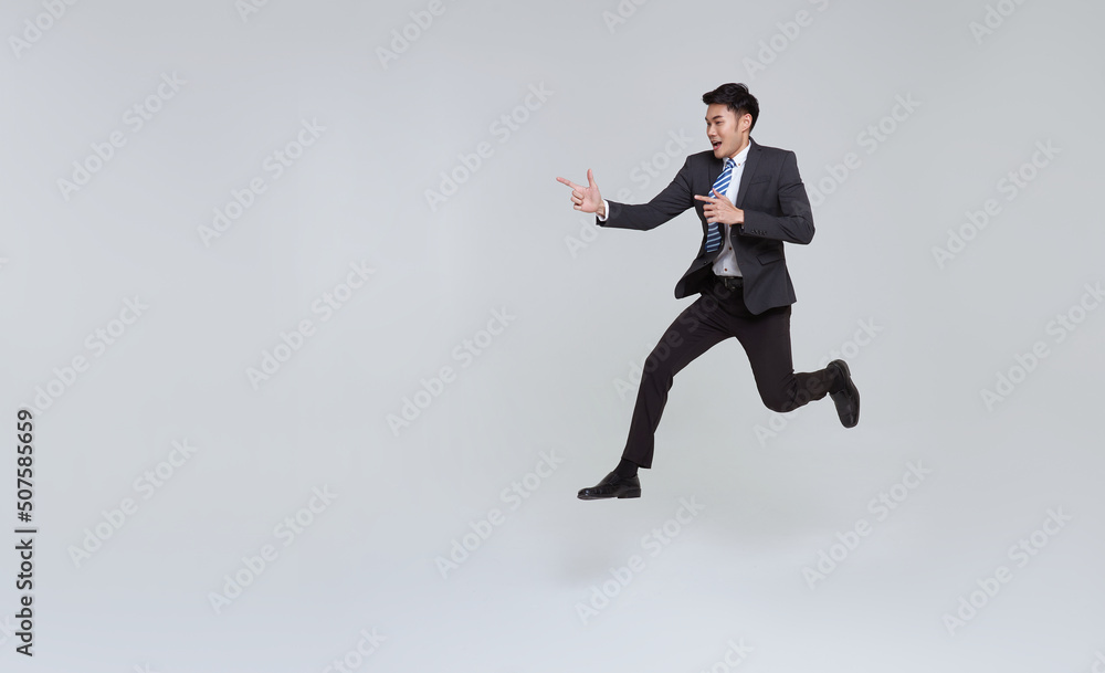 handsome happy energetic young Asian businessman jumping in mid-air and hand pointing isolated on white copy space background.