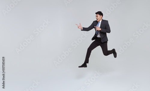 handsome happy energetic young Asian businessman jumping in mid-air and hand pointing isolated on white copy space background.