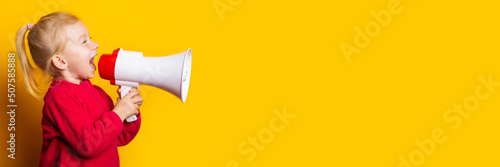 Fototapeta child girl shouts into a white megaphone on a bright yellow background