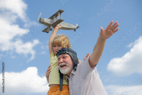 Young grandson and old funny excited grandfather having fun with toy plane on sky. Child dreams of flying, happy childhood with granddad. Generational family.