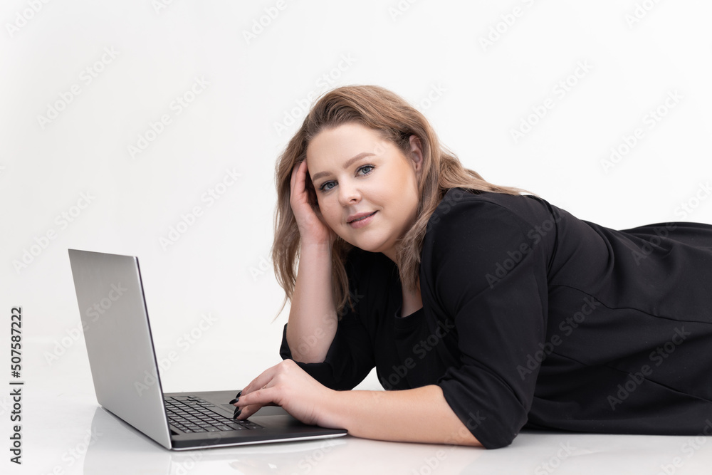 Smiling and thoughtful fair-haired woman lying on floor, using laptop on white background. Freelance and remote work. Smiling and thoughtful fair-haired woman lying on floor, using laptop on white background. Freelance and remote work.