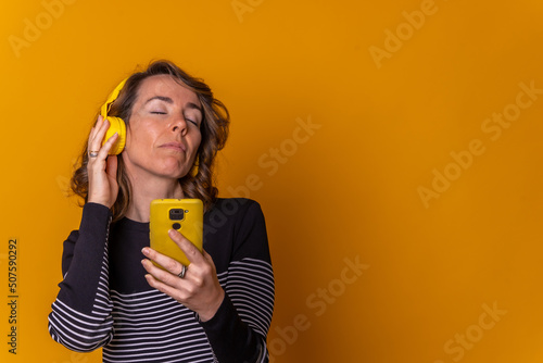 Caucasian girl listening to music with her eyes closed on her phone with headphones, yellow background