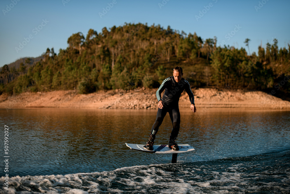 man riding on river water on a foil wakeboard on beautiful landscape background.