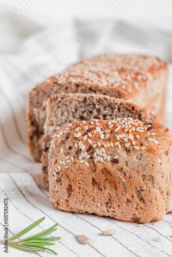 Sliced bread with sesame seeds on a light tablecloth with rosemary. Side view.