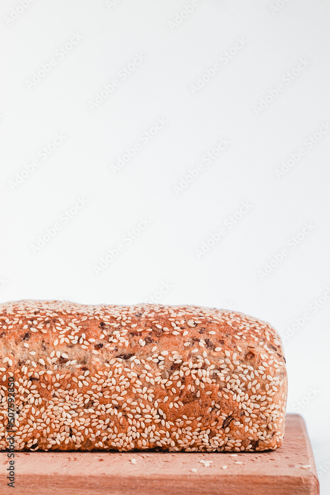Fresh loaf of sesame bread on a wooden board on a white background. Side view. Copy space. Fresh loaf of sesame bread on a wooden board on a white background. Side view. Copy space.