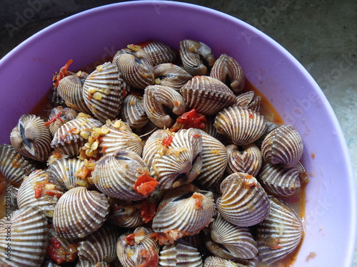  Boiled cockles,  blood clams seasoned with red onion, garlic and cayenne pepper. placed in a purple plastic bowl, top view of hot delicious sauce, Indonesian food