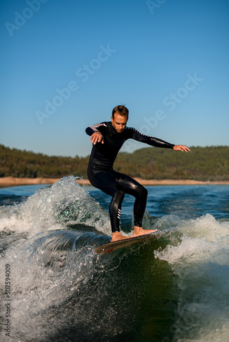 young active man energetically balancing on a wave on a wakesurf board © fesenko