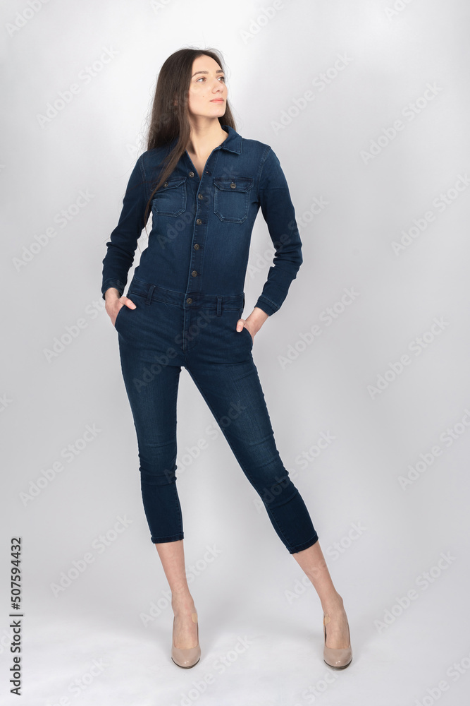 Beauty, fashion and make-up concept. Beautiful slim, tall and sexy looking woman with long hair posing with blue jeans suit in white studio background. Portrait photography. Model looking aside Beauty, fashion and make-up concept. Beautiful slim, tall and sexy looking woman with long hair posing with blue jeans suit in white studio background. Portrait photography. Model looking aside
