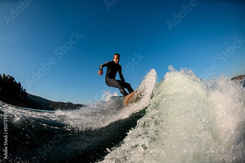 beautiful view of young man riding on a wakesurf board on the splashing wave