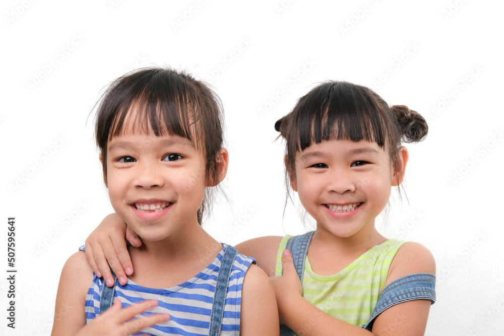 Two little sisters hugging and looking at camera isolated on white background. Two pretty little girls sisters happily cuddle and laugh. friendship and love concept. Two little sisters hugging and looking at camera isolated on white background. Two pretty little girls sisters happily cuddle and laugh. friendship and love concept.