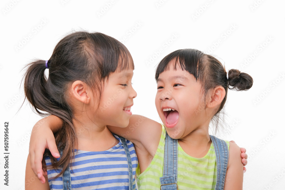 Two little sisters hugging and looking at each other isolated on white background. Two pretty little girls sisters happily cuddle and laugh. friendship and love concept. Two little sisters hugging and looking at each other isolated on white background. Two pretty little girls sisters happily cuddle and laugh. friendship and love concept.