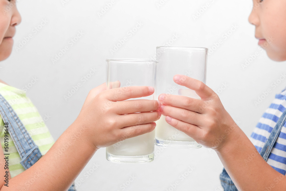 Two little sisters drinking tasty milk from glasses isolated on white background. Happy 6- and 5-year-old sisters drink healthy milk before school. Two little sisters drinking tasty milk from glasses isolated on white background. Happy 6- and 5-year-old sisters drink healthy milk before school.