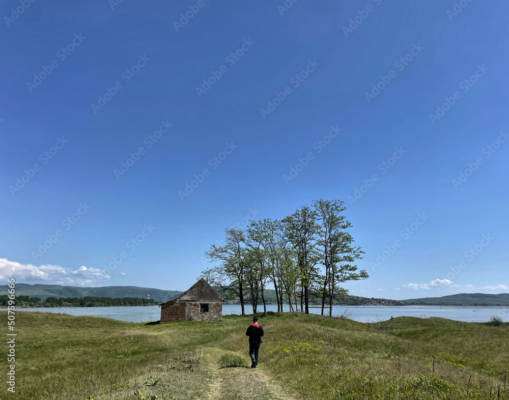 Wanderer (männlich) vor einer alten Hütte mit Baumgruppe am Ufer der Donau in den Dünen der Banater Sandwüste, Vojvodina, Serbien Wanderer (männlich) vor einer alten Hütte mit Baumgruppe am Ufer der Donau in den Dünen der Banater Sandwüste, Vojvodina, Serbien