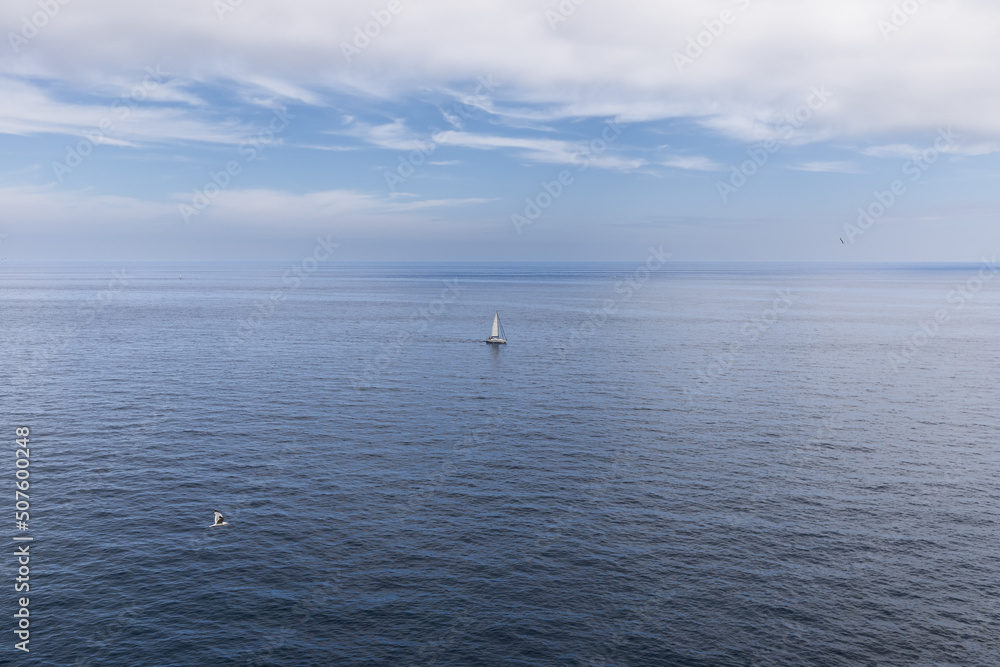 Metaphor for solitude, loneliness and purity: white yacht with white sail, silver gull in flight over Bay of Biscay