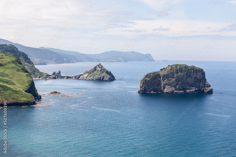 View from Matxitxako lighthouse to 2 little rocky islands Gaztelugatxe and Aketx and part of green coastline with shallow waters of Bay of Biscay, Basque Country, Spain