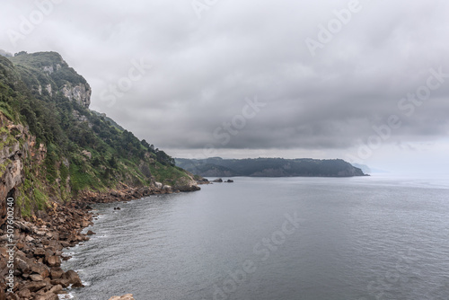 Typical landscape of northern coast of Iberian peninsula - evergreen rocky cliffs, gray sea, low heavy thunderclouds. Cabo de Santa Catalina, Lequeitio, Basque Country
