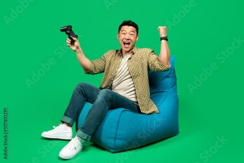 Overjoyed mature male gamer with joystick making YES gesture, feeling happy over victory, sitting in beanbag chair