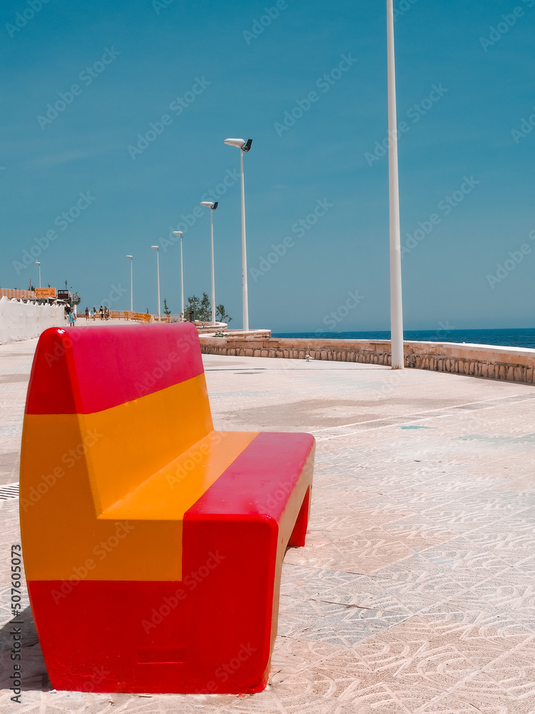 Bench in Spanish colors on the promenade overlooking the sea. The inscription on the promenade 