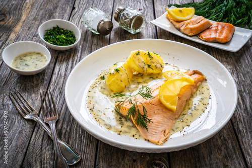 Roasted trout fillet with potatoes and dill sauce served on wooden table 