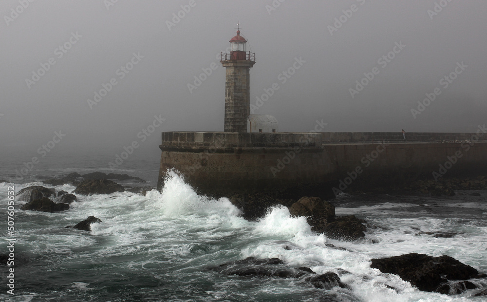 Lighthouse and ocean waves breaking against the rocks in Porto Portugal, dramatic scenery before the storm, side view