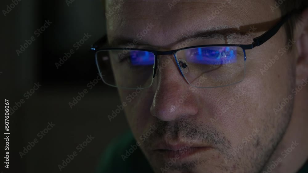 Close-up portrait of millennial concentrated trader man in glasses looks at screen with graphs in dark. Caucasian man analyst monitors exchange rate on tablet reflection in eyeglasses. Close-up portrait of millennial concentrated trader man in glasses looks at screen with graphs in dark. Caucasian man analyst monitors exchange rate on tablet reflection in eyeglasses.