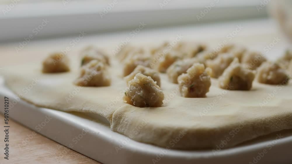 Close-Up Of Female Hands Making Dumplings With Minced Meat. With our hands, we spread the meat filling into the dough, a form for dumplings. Traditional Russian cuisine. Cooking homemade food.Ravioli Close-Up Of Female Hands Making Dumplings With Minced Meat. With our hands, we spread the meat filling into the dough, a form for dumplings. Traditional Russian cuisine. Cooking homemade food.Ravioli