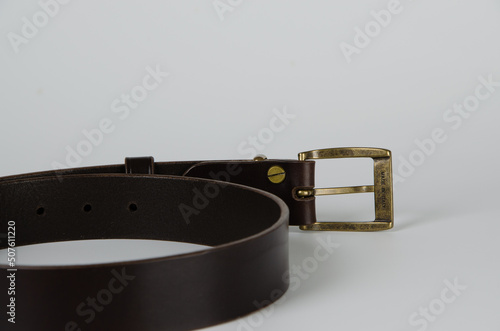 brown Italian leather belt with brass buckle and brass screws on a light background