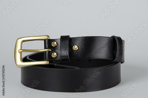 black Italian leather belt with brass buckle and brass screws on a light background