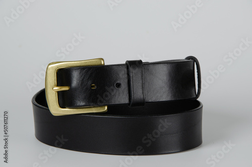black Italian leather belt with brass buckle and brass screws on a light background