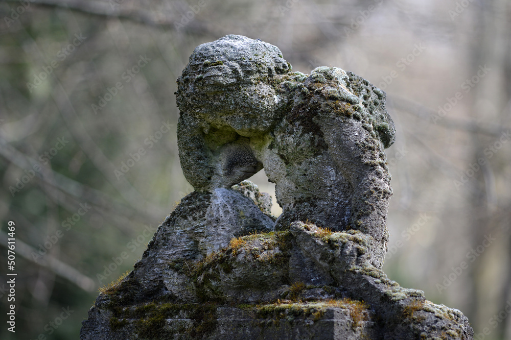 A very old, weathered and with moss covered male sandstone angel in front of a blurred gray background. A very old, weathered and with moss covered male sandstone angel in front of a blurred gray background.