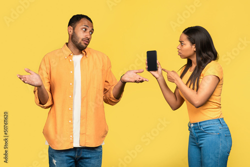 Angry black woman showing smartphone with mockup to her boyfriend, blaming him for using online dating app